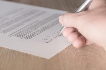 Dokument i składany na niej podpis odręczny (widoczny fragment dłoni trzymającej długopis) 