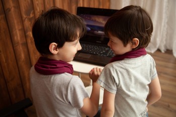 Dwoje uśmiechniętych dzieci spogląda na siebie. W tle widoczny pulpit i klawiatura laptopa.